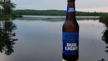 En Bud Light-ølflaske på en moler med en sø og skov i baggrunden.