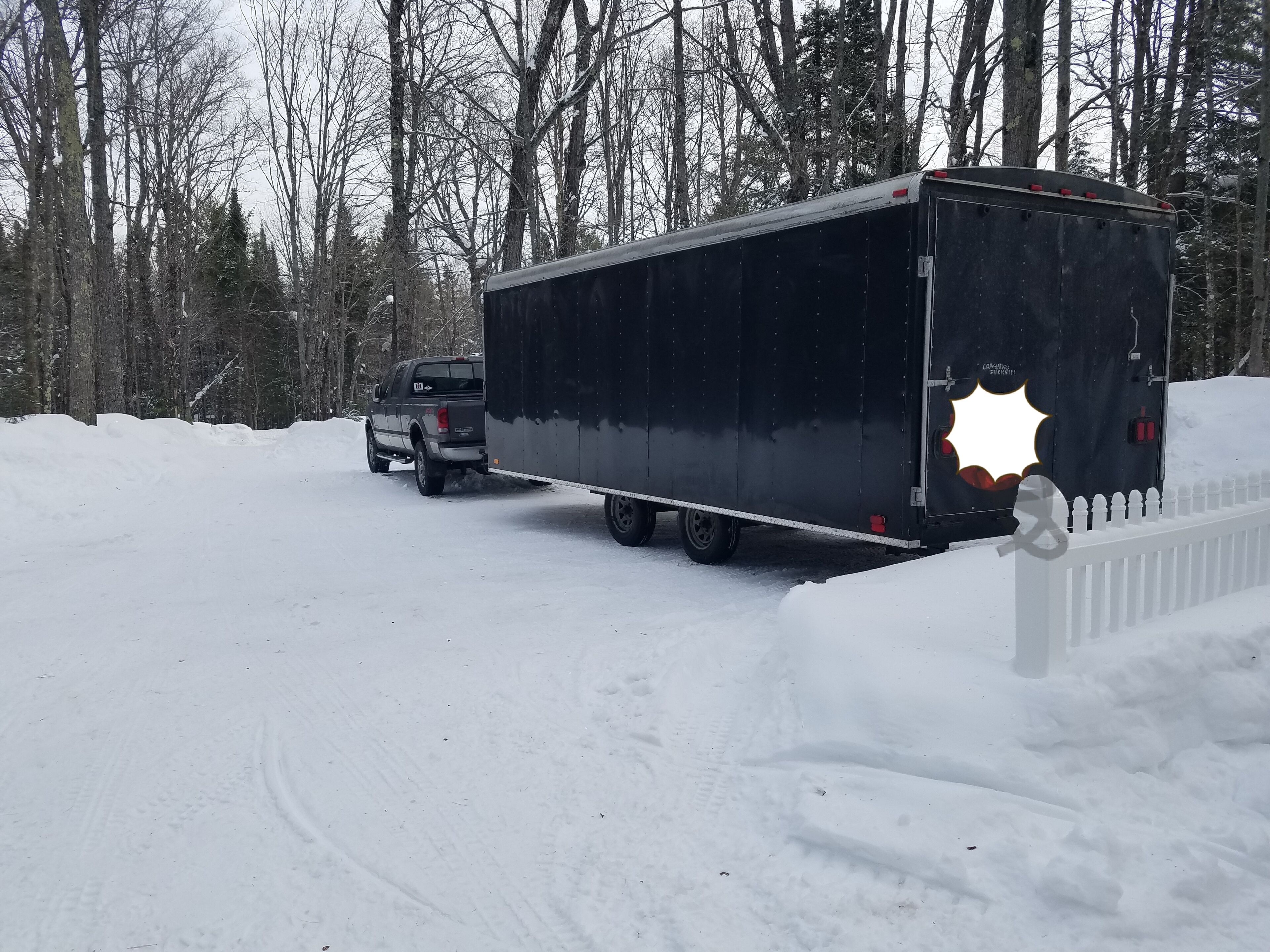 A truck with a trailer parked on a snow-covered road.