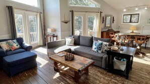 A spacious living room with a sofa, a coffee table, and a dining area with wooden chairs and a table. - Bearfoot Bodega: Pet friendly on Back Road near the Coffee Co. (Ocracoke)
