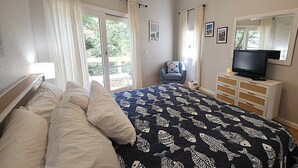 A bedroom with a bed, a TV, a dresser, and a chair. - Bearfoot Bodega: Pet friendly on Back Road near the Coffee Co. (Ocracoke)