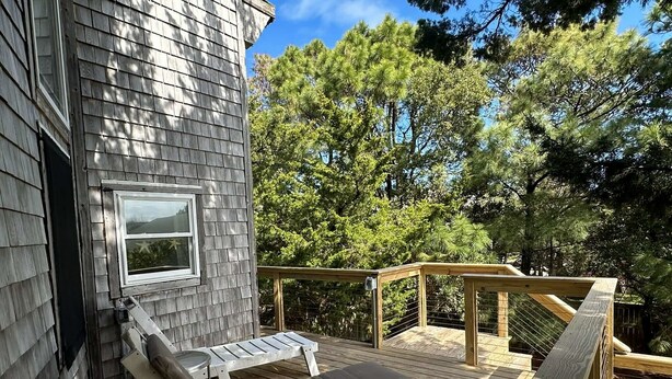 A wooden deck with two lounge chairs and a small table, surrounded by trees. - Bearfoot Bodega: Pet friendly on Back Road near the Coffee Co. (Ocracoke)