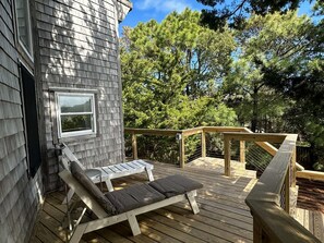 Une terrasse en bois avec deux chaises longues et une petite table, entourée d’arbres.