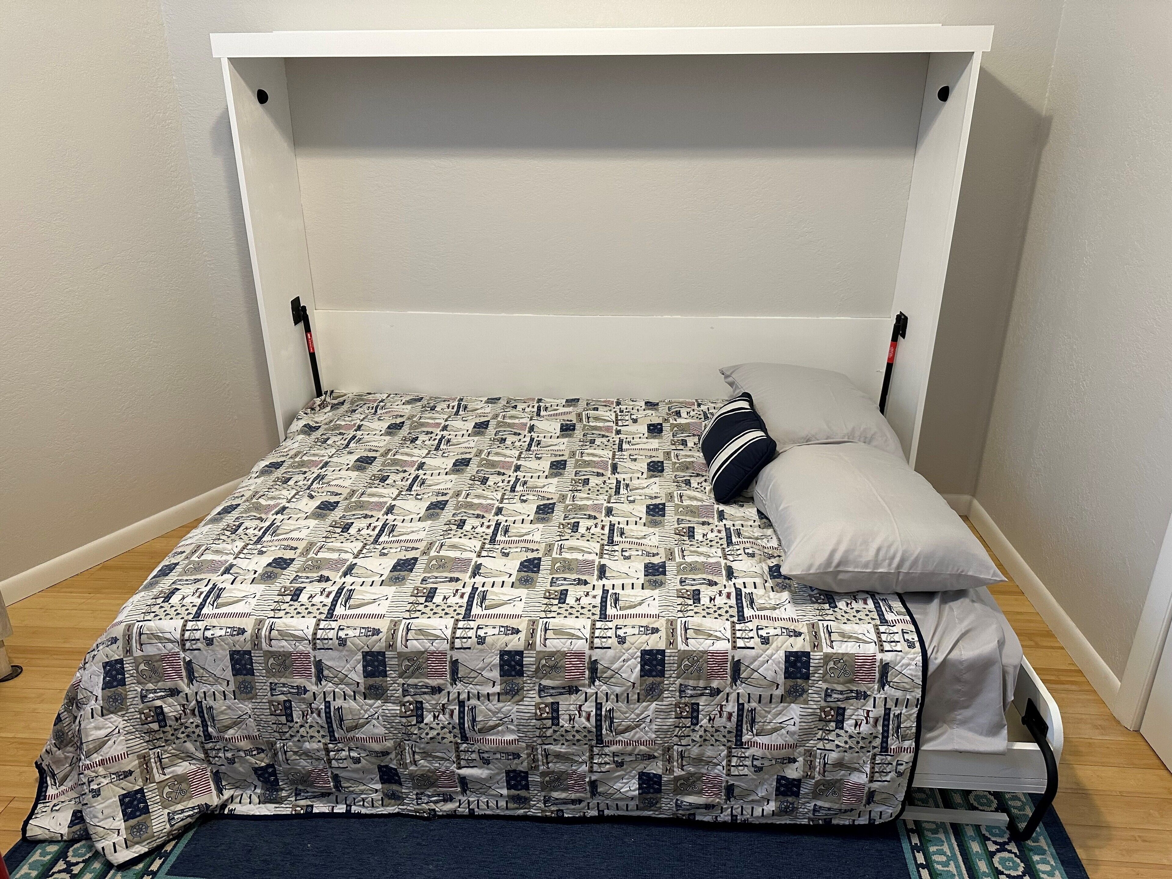 A small, single-bed room with a quilted bedspread featuring a pattern of flags and military symbols.