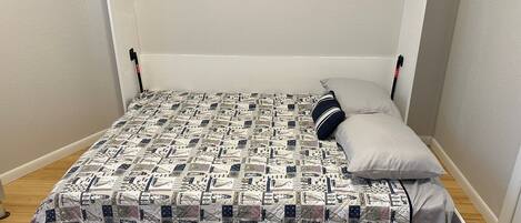 A small, single-bed room with a quilted bedspread featuring a pattern of flags and military symbols.