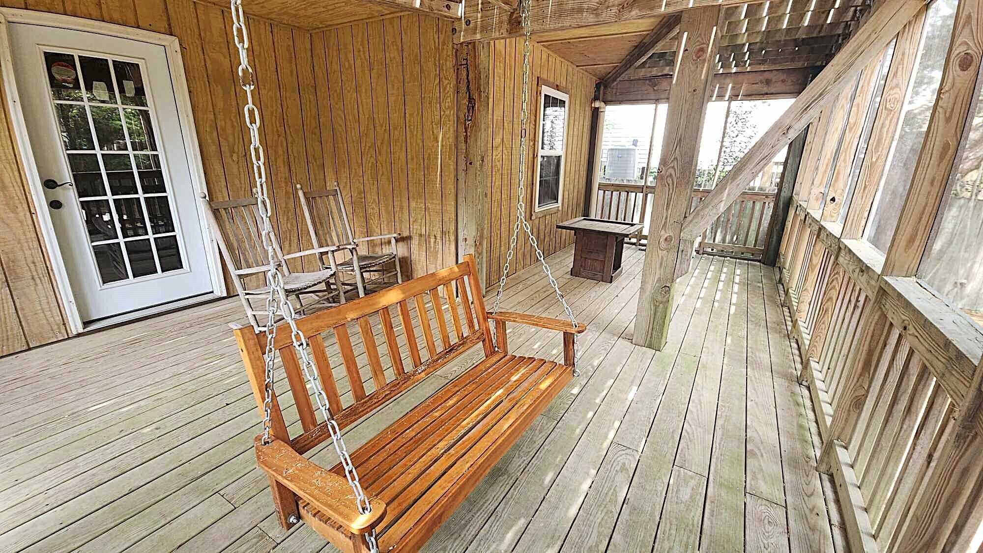 Une terrasse en bois avec une chaise suspendue en bois, un banc et une table.