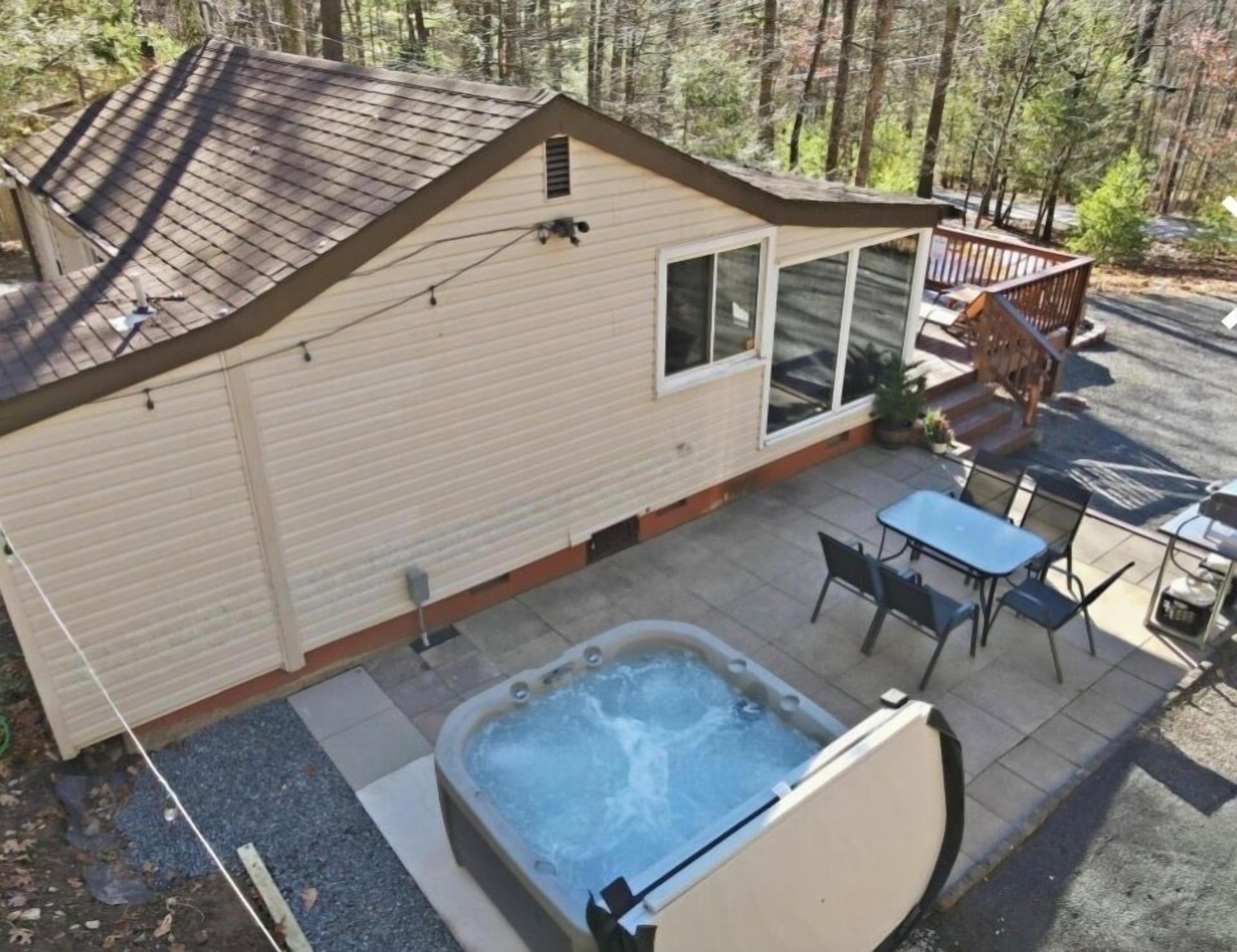 A small cabin with a hot tub, patio seating, and a deck.