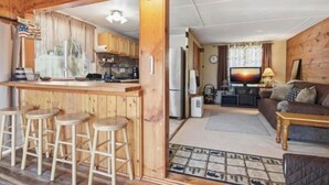 L’intérieur d’une cabane en bois comprend une cuisine, un coin bar avec des tabourets, un salon avec un canapé et une télévision, ainsi qu’un coin repas.