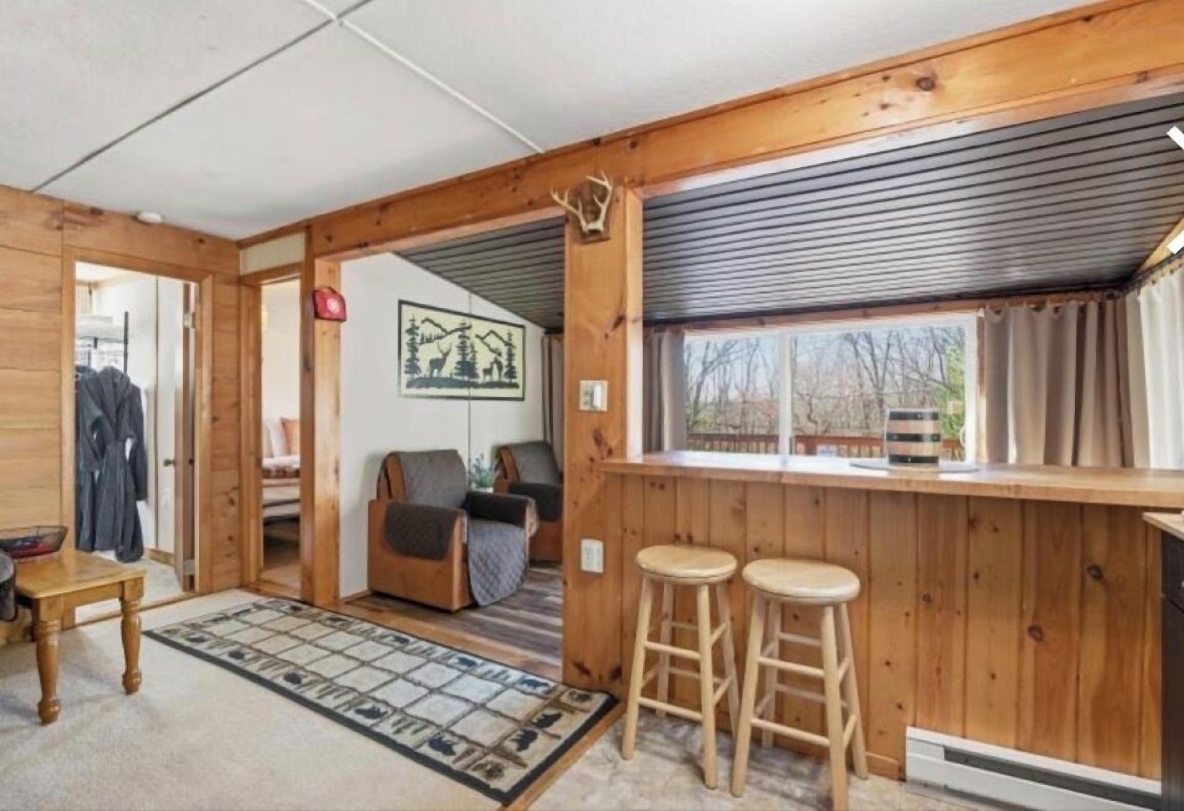 L’intérieur d’un chalet en bois, avec un coin salon confortable, un comptoir de bar avec des tabourets et une grande fenêtre.