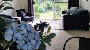 A living room with a dining table, two sofas, a chandelier, and a view of a garden through a sliding glass door. - 'Little Britton' self contained accommodation (Wingham)