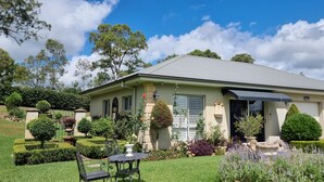 A two-story house with a well-maintained garden, a patio with a table and chairs, and a covered entryway. - 'Little Britton' self contained accommodation (Wingham)