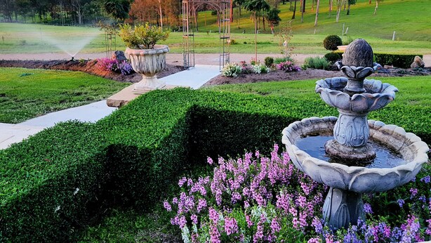 A well-maintained garden with a central pathway, a decorative fountain, and a pergola structure. - 'Little Britton' self contained accommodation (Wingham)