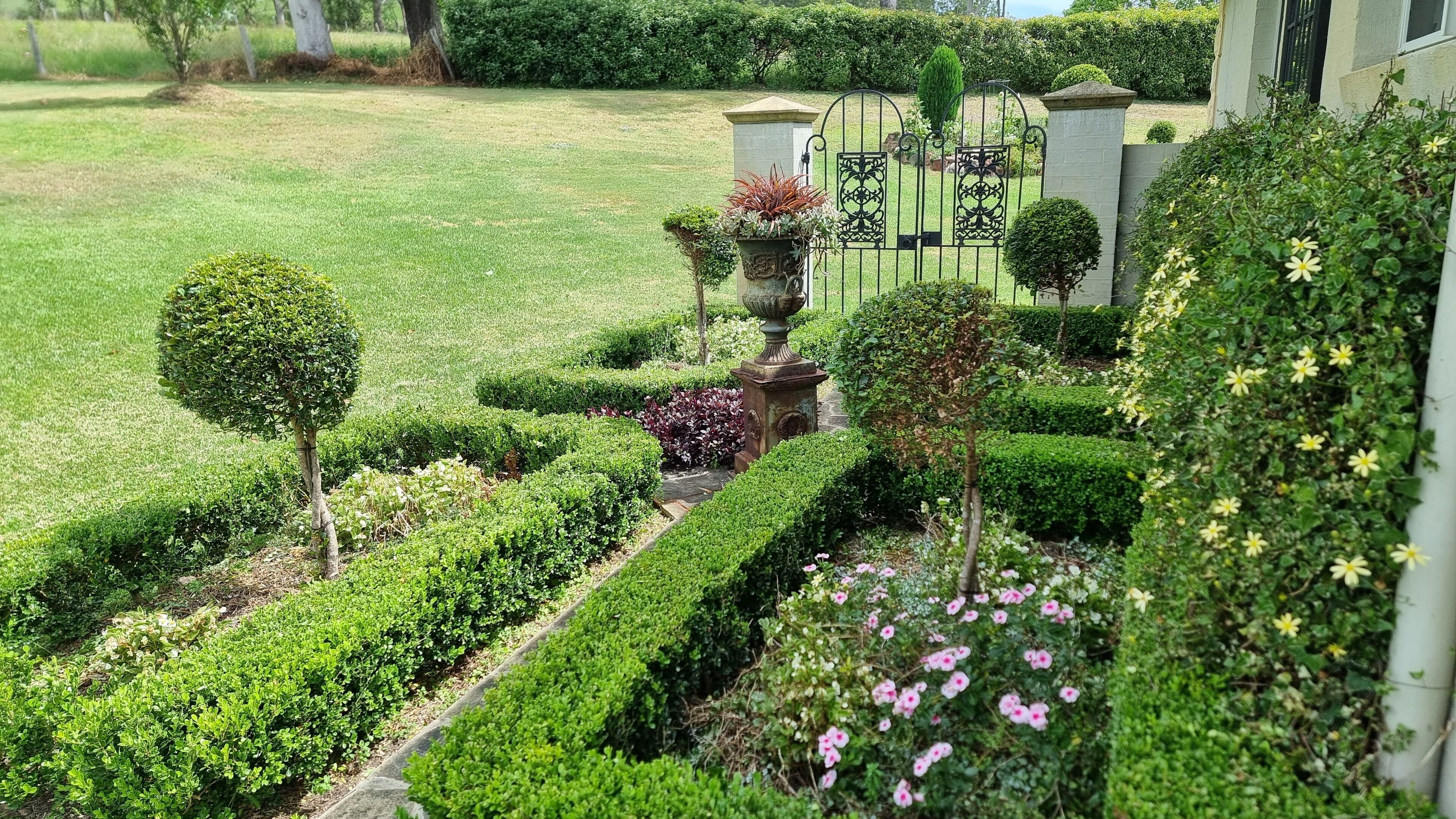 A well-maintained garden with neatly trimmed hedges, a variety of flowering plants, and a decorative urn.