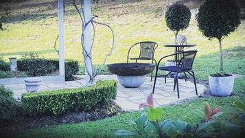 A patio with a table and chairs, surrounded by well-maintained hedges and a small tree.