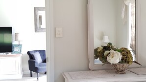 A room with a white dresser, a mirror, and a vase of flowers. There is a chair and a television in the background. - 'Little Britton' self contained accommodation (Wingham)