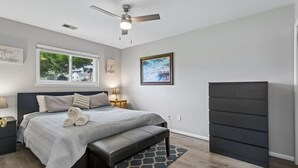 A bedroom with a bed, a bench, a ceiling fan, a dresser, and a window. - Full Condo w/ pool, 5 min walk to beach (Virginia Beach)