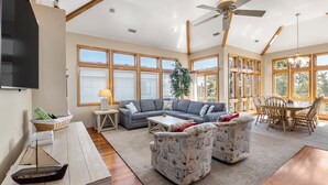 A spacious living room with a large sofa, two patterned armchairs, a wooden coffee table, and a dining table with chairs.