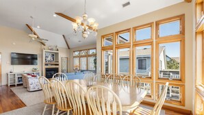 A spacious dining area with a large round table and multiple chairs, a ceiling fan, and a chandelier.