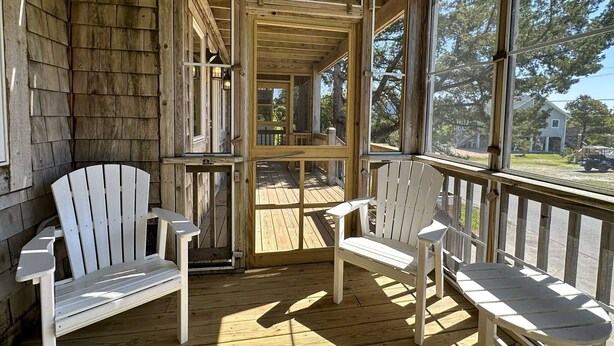 A wooden porch with two Adirondack chairs, a wooden deck, and a view of a residential area.