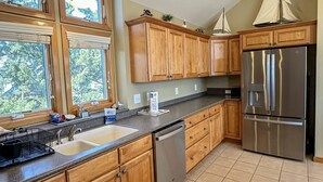 A kitchen with wooden cabinets, a stainless steel refrigerator, a dishwasher, and a window with a view of trees.