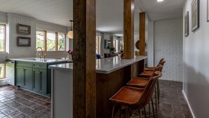 Eine Küche mit einer zentralen Kochinsel, Holzsäulen, Barhocker und einer Wand aus weißen Ziegelsteinen.
