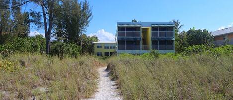 A pathway leading to a building with multiple balconies and a yellow facade.