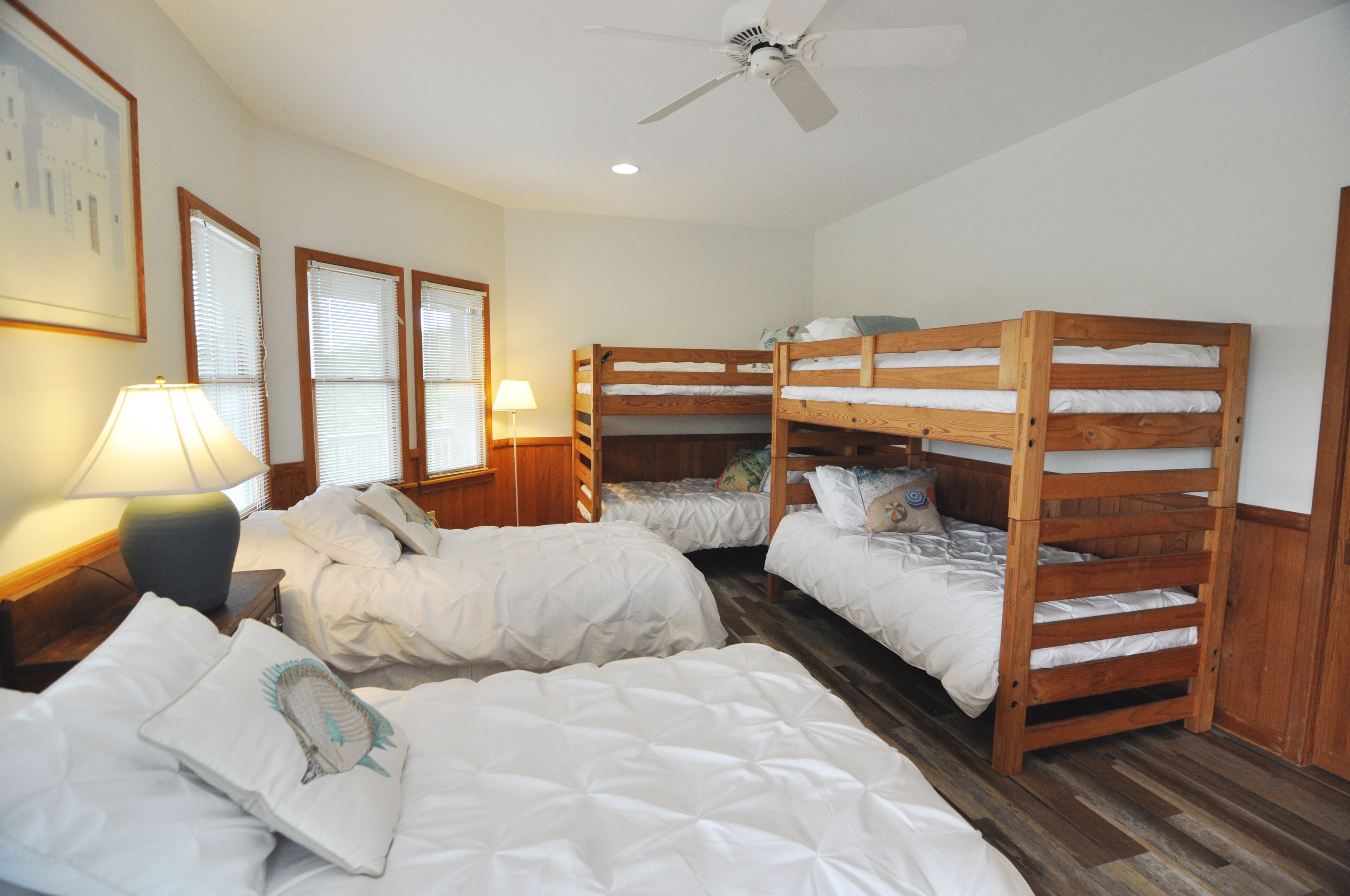 A room with bunk beds, a ceiling fan, and a lamp on a bedside table.