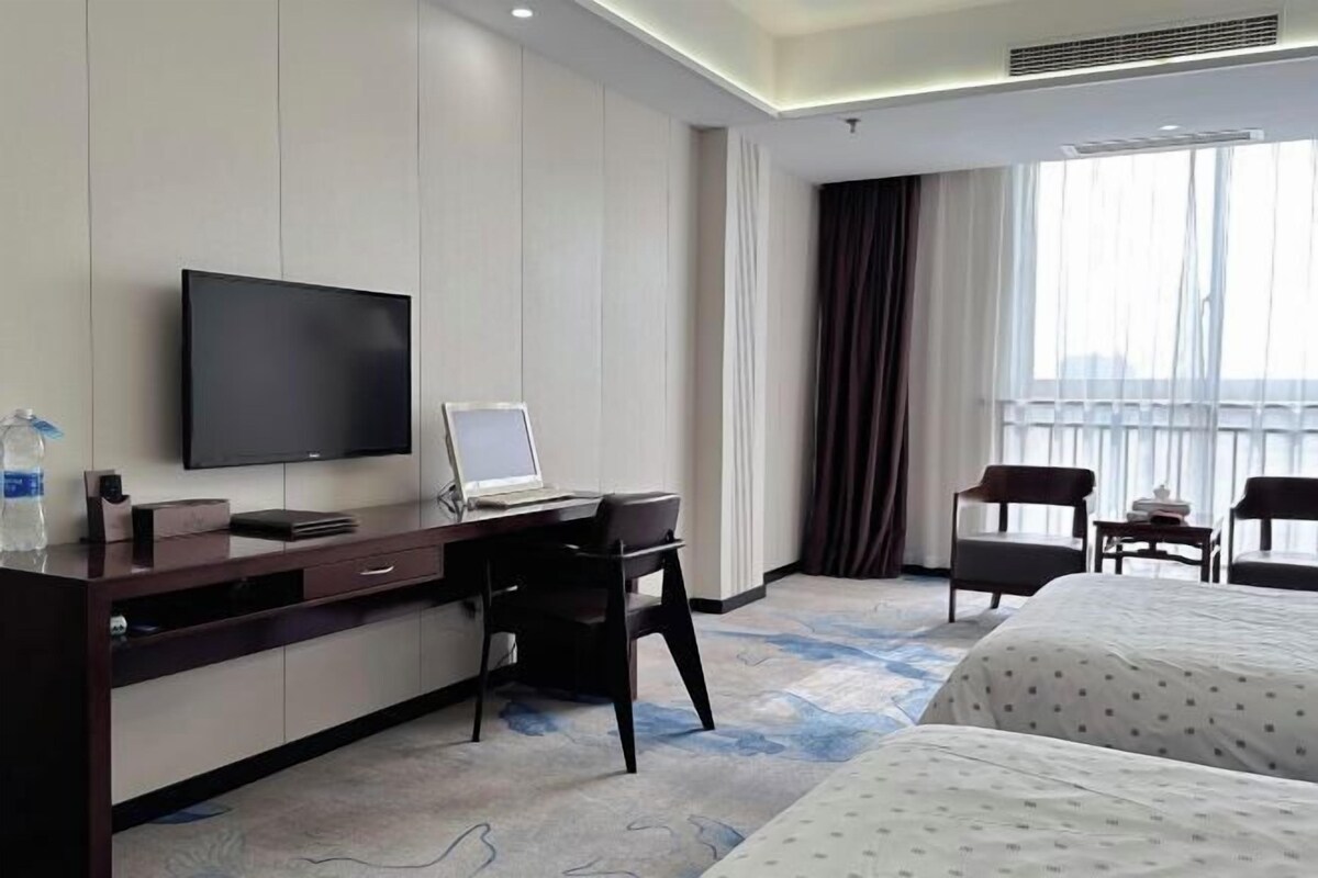 Una habitación de hotel con una cama, un escritorio con computadora, un televisor y dos sillas.