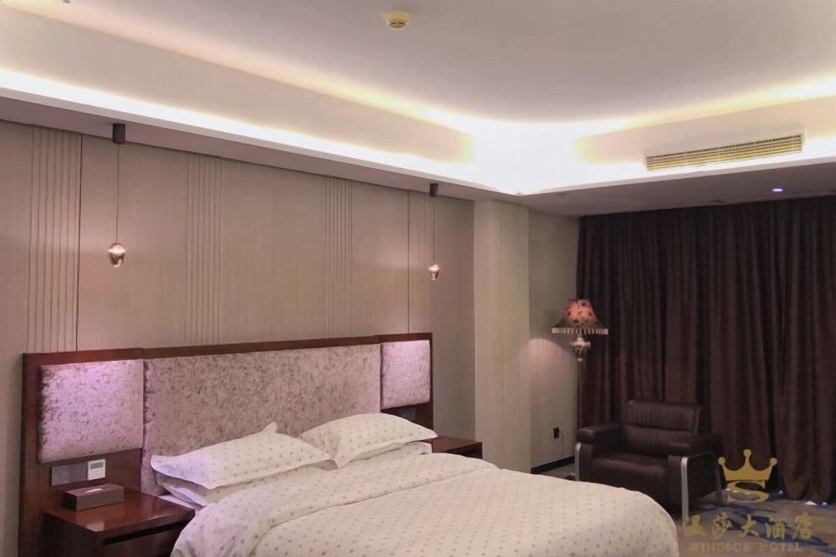 Habitación de hotel con una cama grande, una mesita de noche, una lámpara, una silla y una cortina.