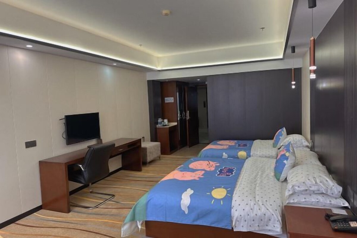 Habitación de hotel con dos camas, un escritorio, un televisor y un baño visible a través de una puerta abierta.