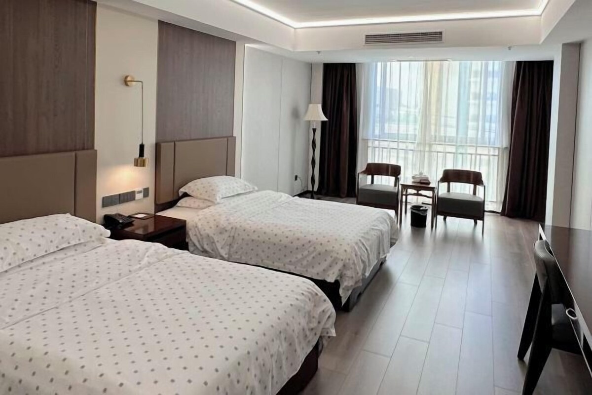 Habitación de hotel con dos camas, un escritorio, una silla y una ventana con cortinas.