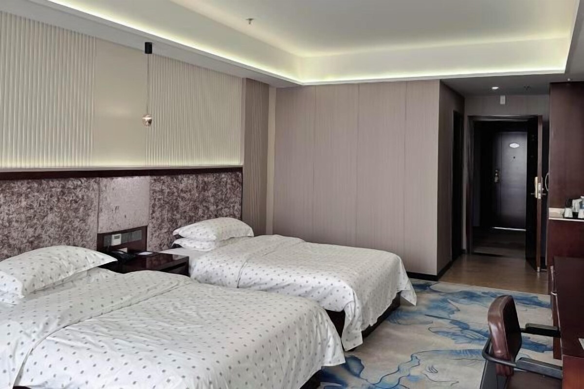 Ett hotellrum med två sängar, en sänggavel i marmor, ett nattduksbord i trä och ett badrum som syns genom en öppen dörr.