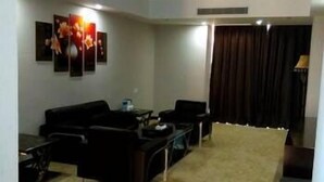 A living room with a sofa set, a coffee table, and a TV. There are framed pictures on the wall and a curtain on the window. - Windsor Hotel (Zhangzhou)