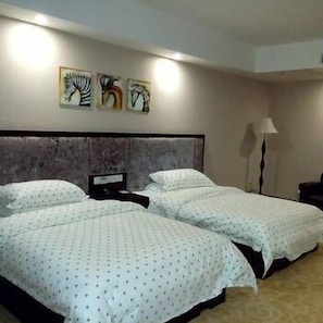 Habitación de hotel con dos camas, cabecera, mesita de noche, lámpara y tres obras de arte en la pared.