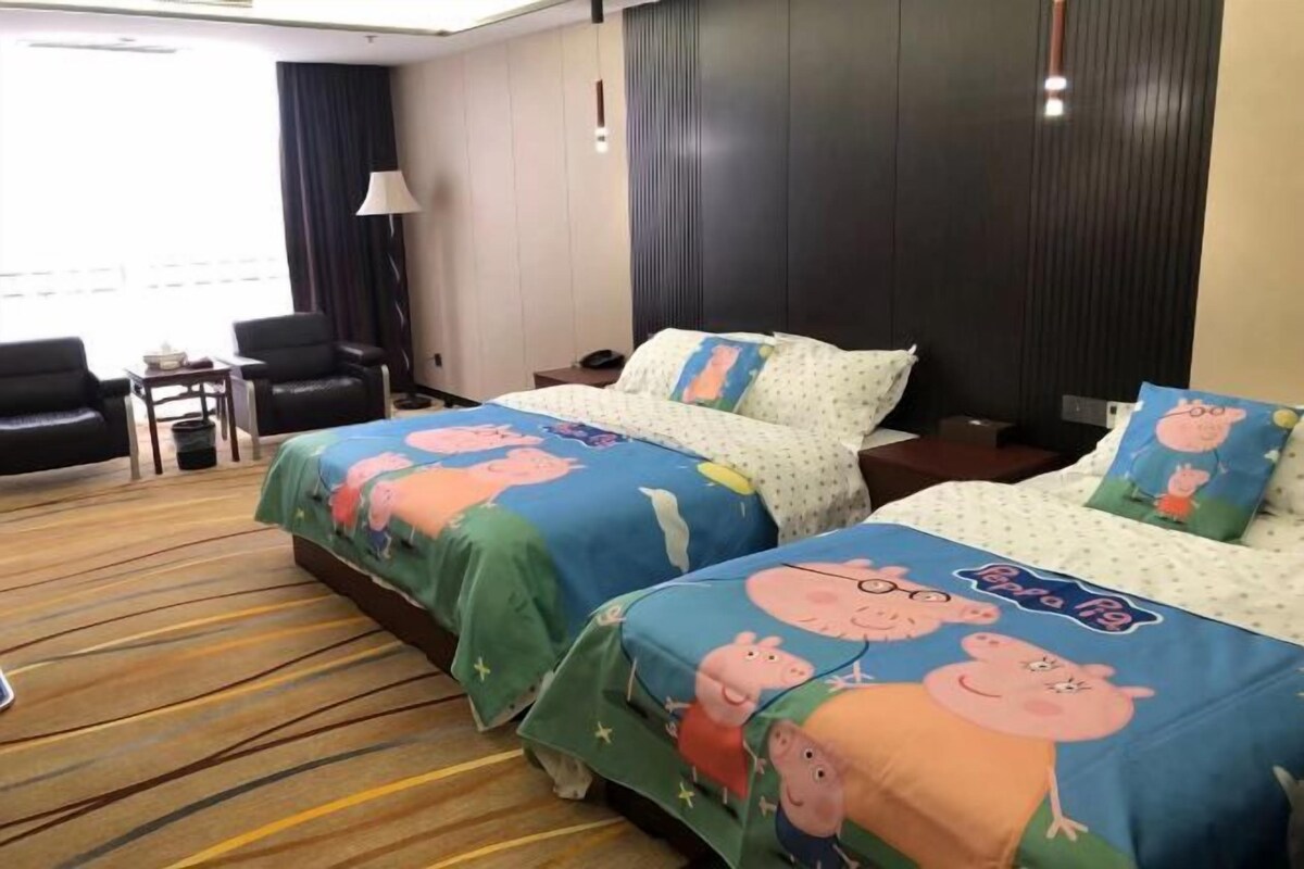 A hotel room with two beds, each with a 'Peppa Pig' themed bedspread. There are two chairs and a small table in the room.