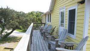 Une terrasse en bois avec plusieurs chaises Adirondack, une petite table et une rambarde.