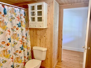 Kylpyhuoneessa on puulattia, wc-istuin, kalan kuvioilla varustettu suihkuverho ja wc-istuimen yläpuolella oleva kaappi.
