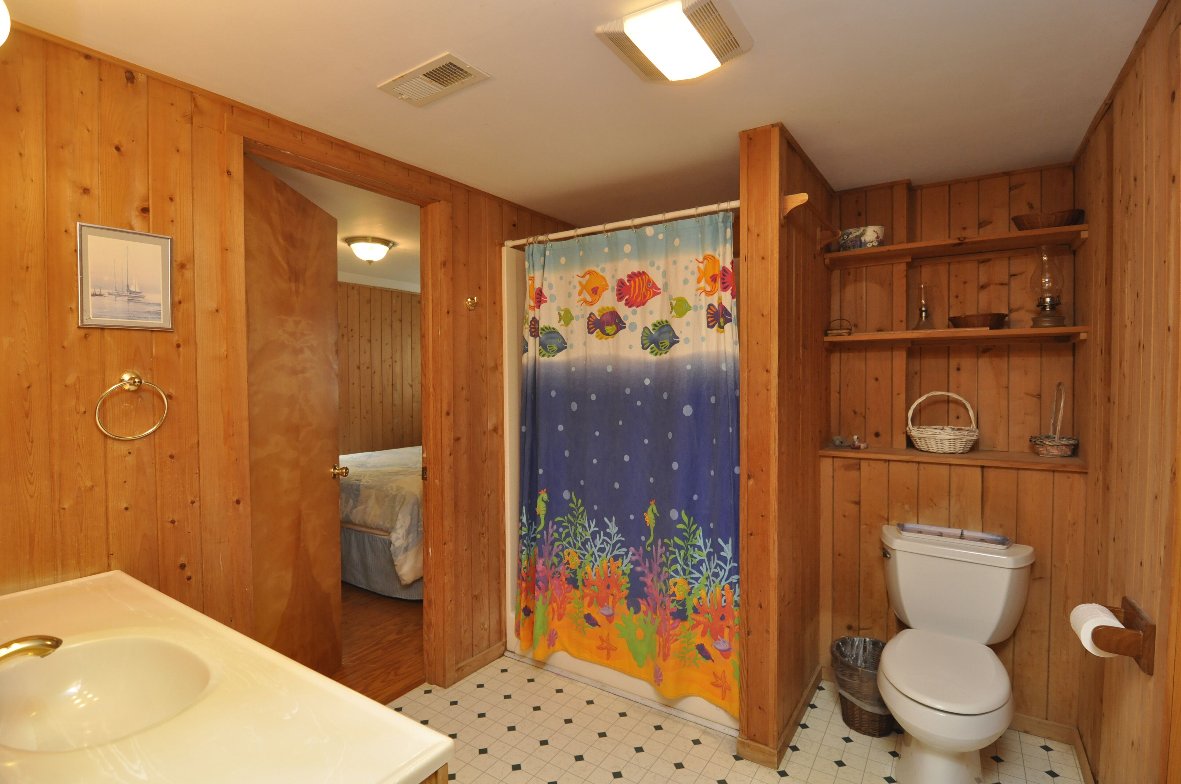A wooden bathroom with a white sink, a toilet, and a shower curtain with a fish design.