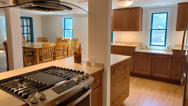 Une cuisine moderne avec des meubles en bois, une cuisinière en acier inoxydable et un coin repas avec des chaises en bois.