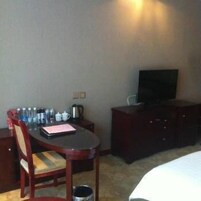 Habitación de hotel con una cama, un televisor sobre un mueble, una mesa con una silla y un pequeño escritorio con una tetera y tazas.