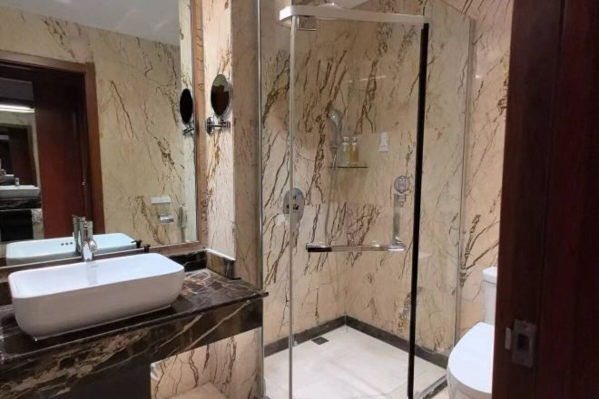 Un baño con un espejo grande, un lavabo blanco, ducha con cerramiento de vidrio y paredes de mármol.