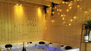 Een houten hut met een hottub, sfeerverlichting en een bankje.
