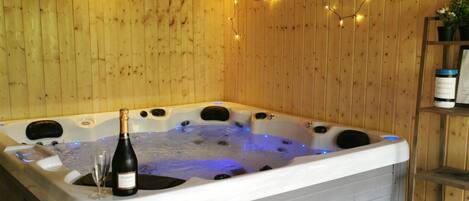 A wooden cabin with a hot tub, string lights, and a bench.