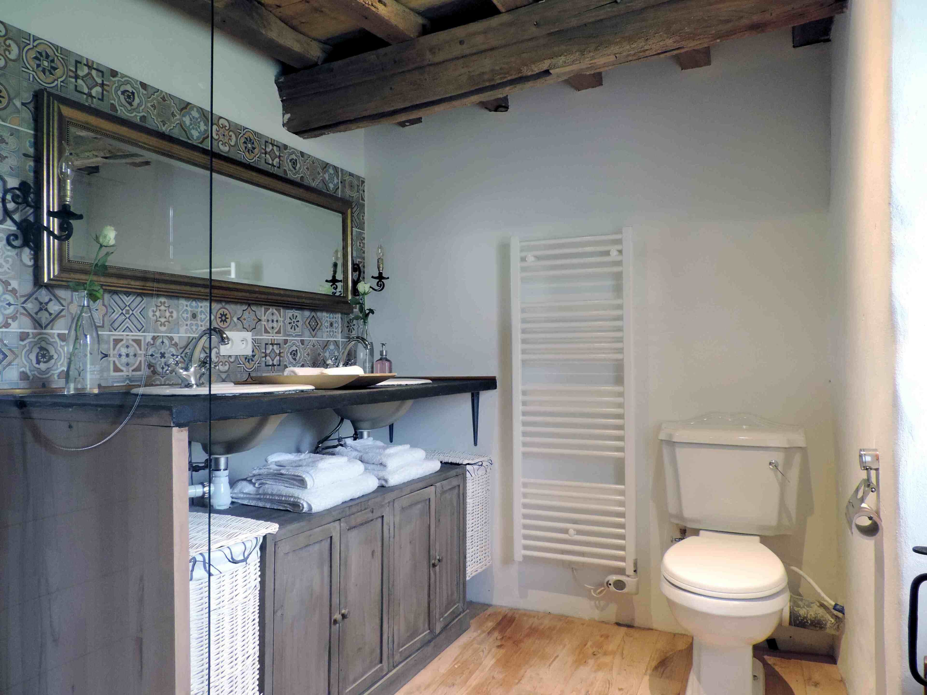 A bathroom with a tiled backsplash, a wooden vanity, a white toilet, and a towel rack.