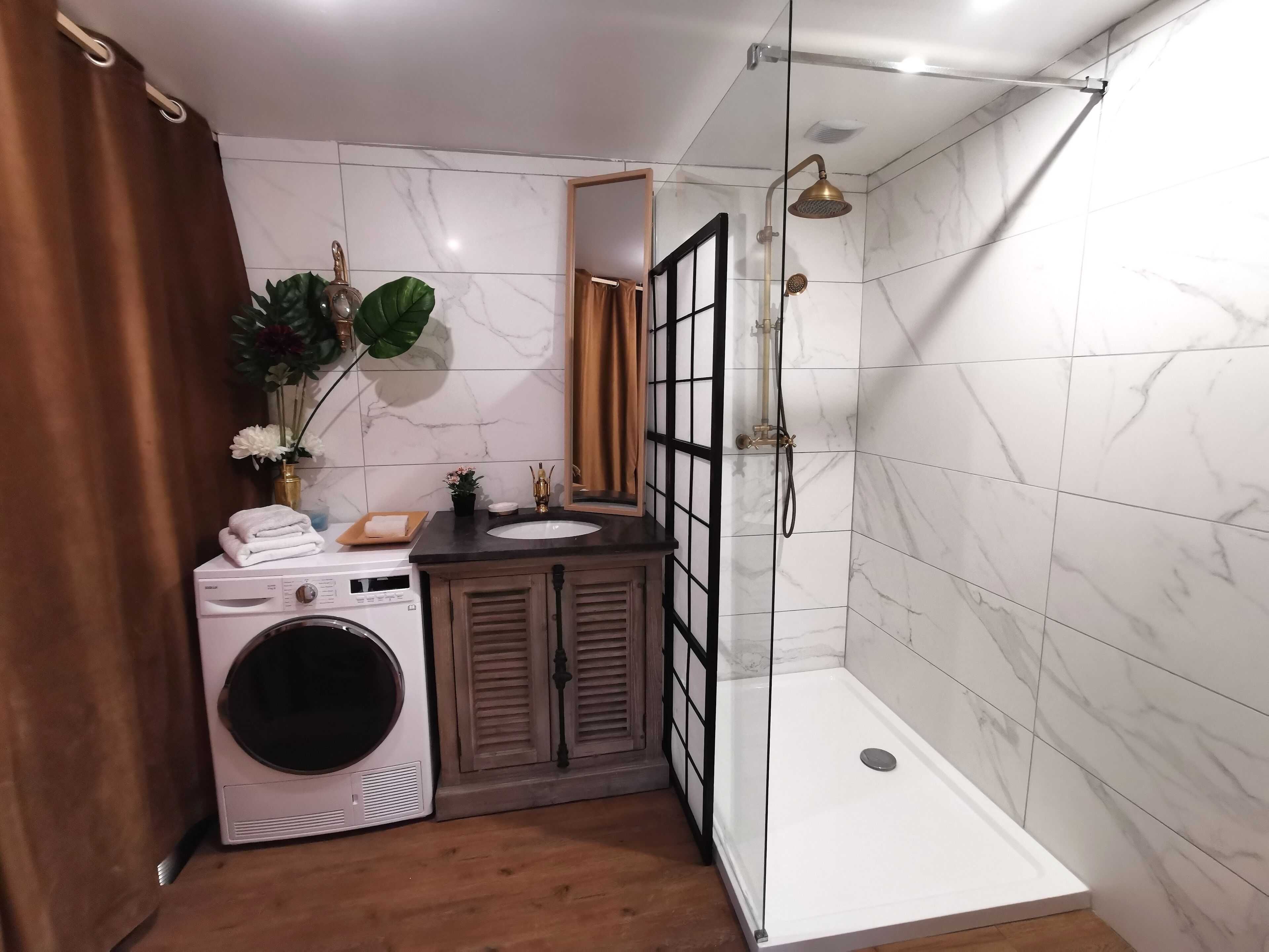 A modern bathroom with a built-in washing machine, a sink, a shower with a glass enclosure, and a large mirror.