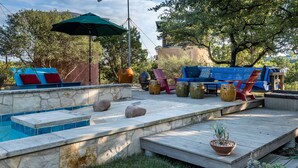 Eine Terrasse mit Steinmauer, Holzdeck, Schwimmbad und Gartenmöbeln.