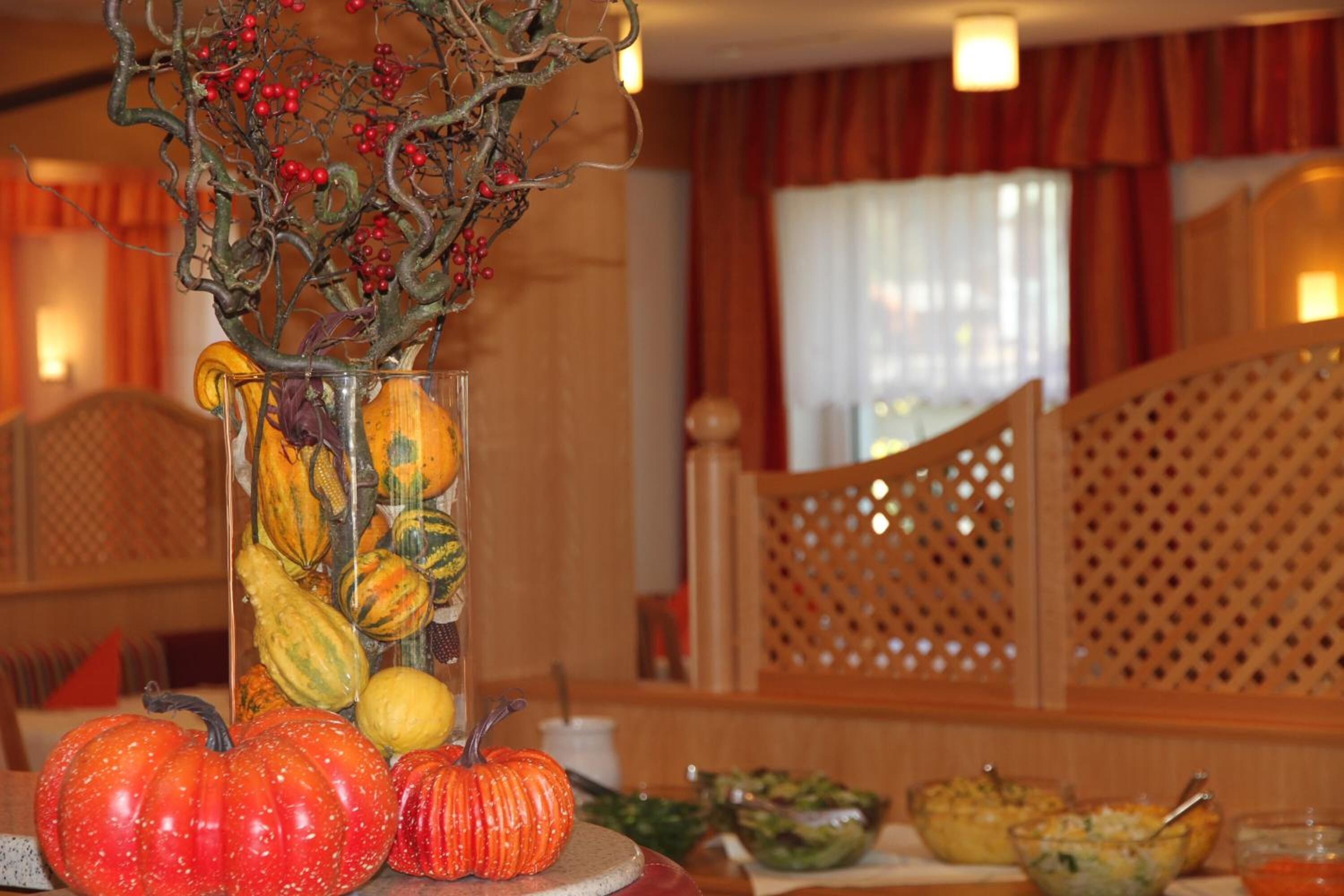 A dining table with a centerpiece of a vase containing autumn leaves and pumpkins, surrounded by various dishes.