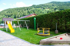 Une aire de jeux avec un toboggan, des balançoires et une structure d’escalade circulaire.