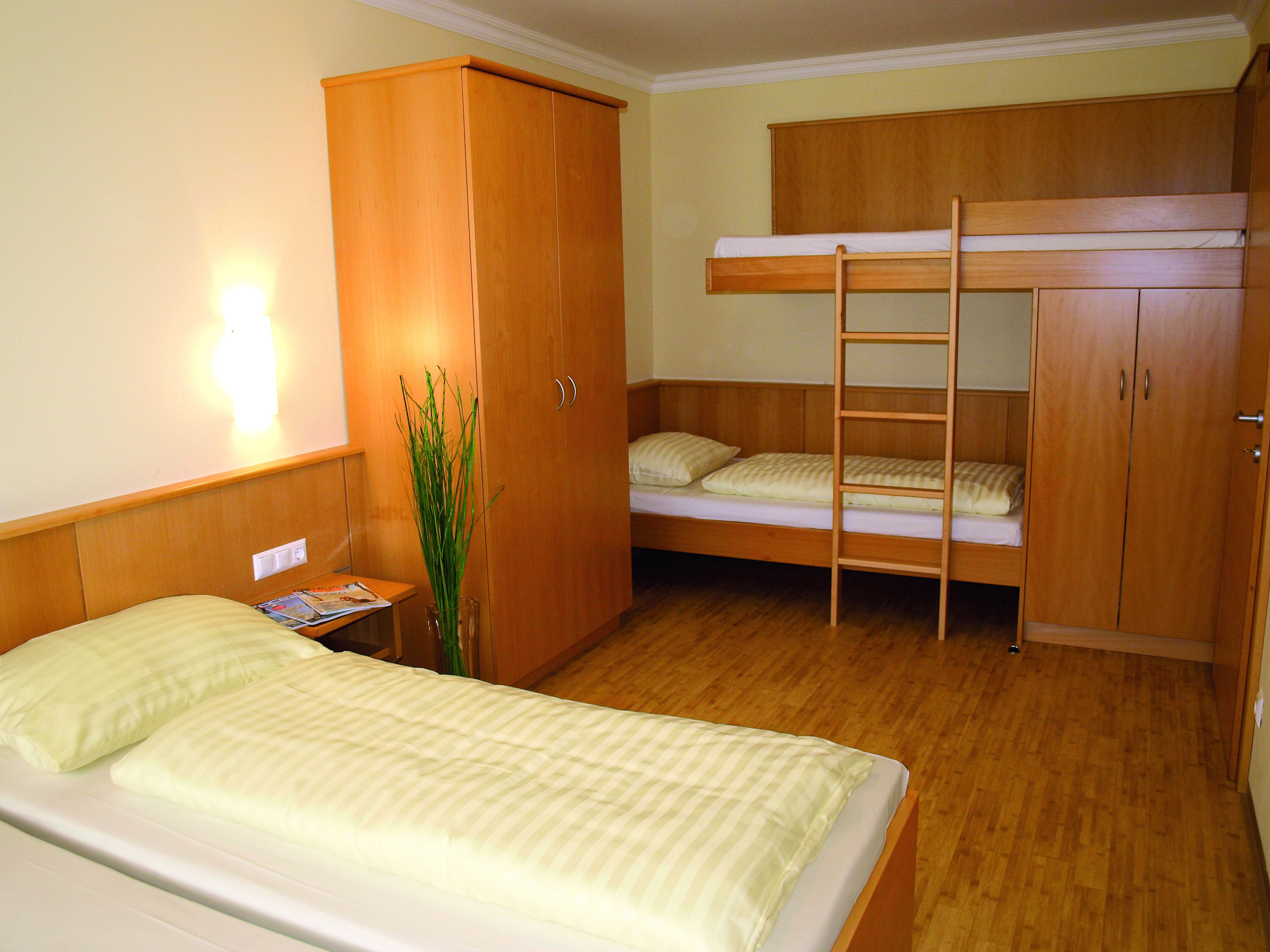 Une petite chambre comprenant un lit superposé, un lit simple et une armoire.