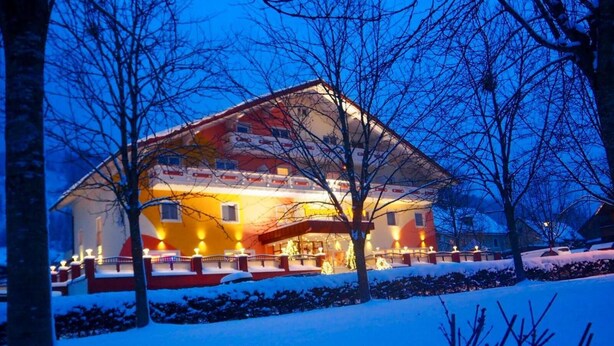 Un grand chalet, bien éclairé, avec un toit enneigé et une entrée lumineuse.