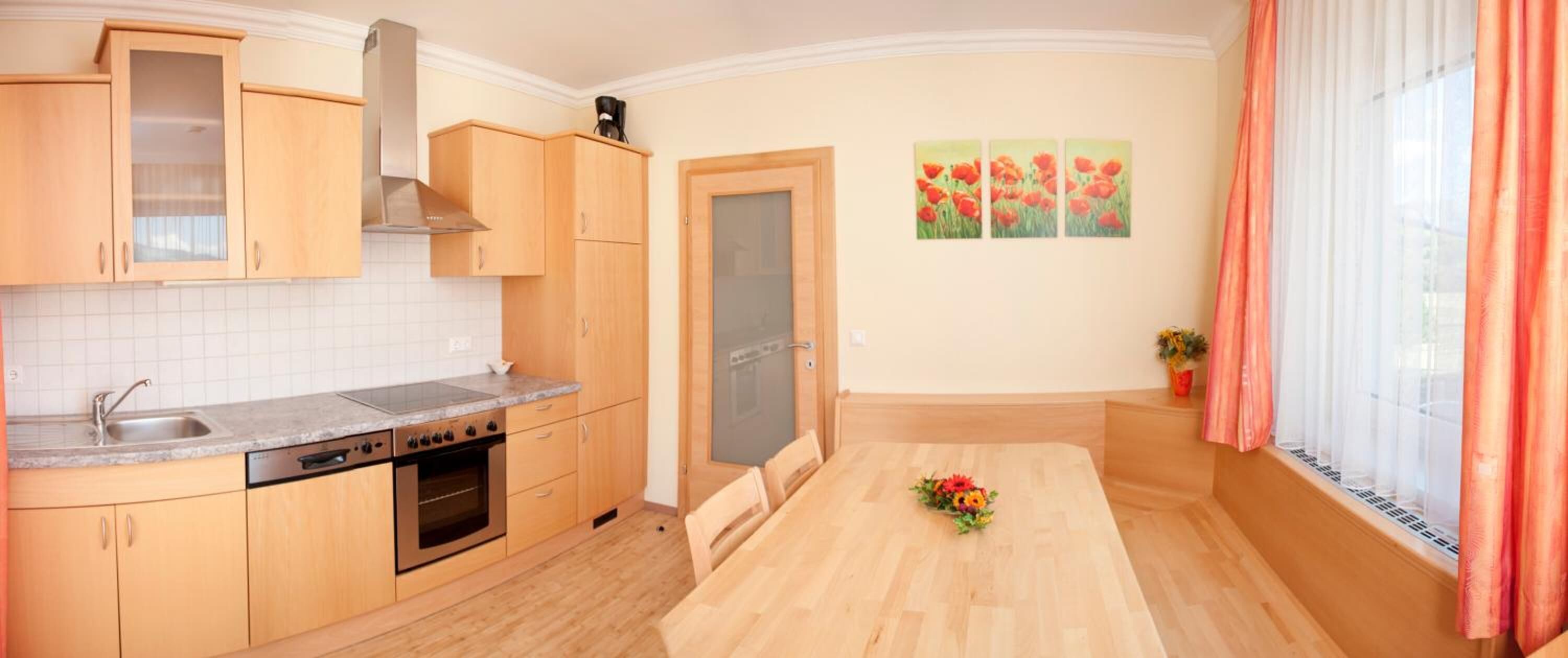 A kitchen with wooden cabinets, a built-in oven, and a dining table with a vase of flowers.